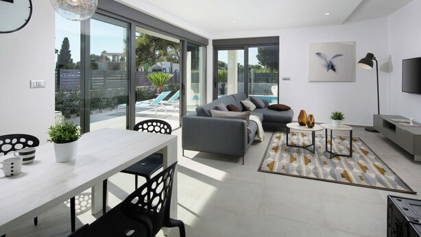A modern living room with a grey sofa, a dining table, and a large window overlooking a pool. - Luxury Apartment With Private Pool, Near the Beach and Close to Pula (Fazana)