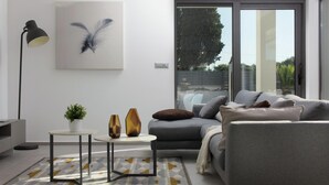 A modern living room with a grey sofa, a small side table with a plant, a floor lamp, and a large window with a view of greenery. - Luxury Apartment With Private Pool, Near the Beach and Close to Pula (Fazana)