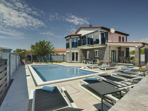 Une maison moderne à deux étages, dotée d’une piscine, d’un espace extérieur aménagé et d’une façade en pierre.