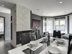 Un espace repas moderne agrémenté d’un mur en pierre, d’un téléviseur à écran plat et offrant une vue sur l’extérieur.