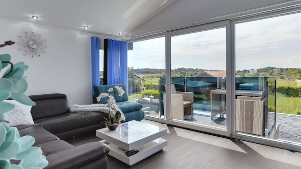 Ein modernes Wohnzimmer mit einer Couch, einem Couchtisch und Blick auf eine grüne Landschaft durch große Glasfenster.