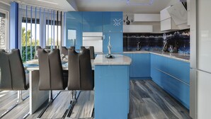 Eine moderne Küche mit blauen Schränken, einer zentralen Kochinsel und einem Essbereich mit Stühlen.