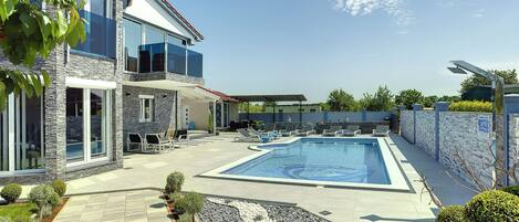 Une maison moderne à deux étages, dotée d’une piscine, d’un espace extérieur aménagé et d’un jardin bien entretenu.