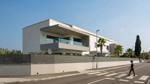 Un edificio moderno de dos plantas con balcones, un paso de peatones y cielo despejado.
