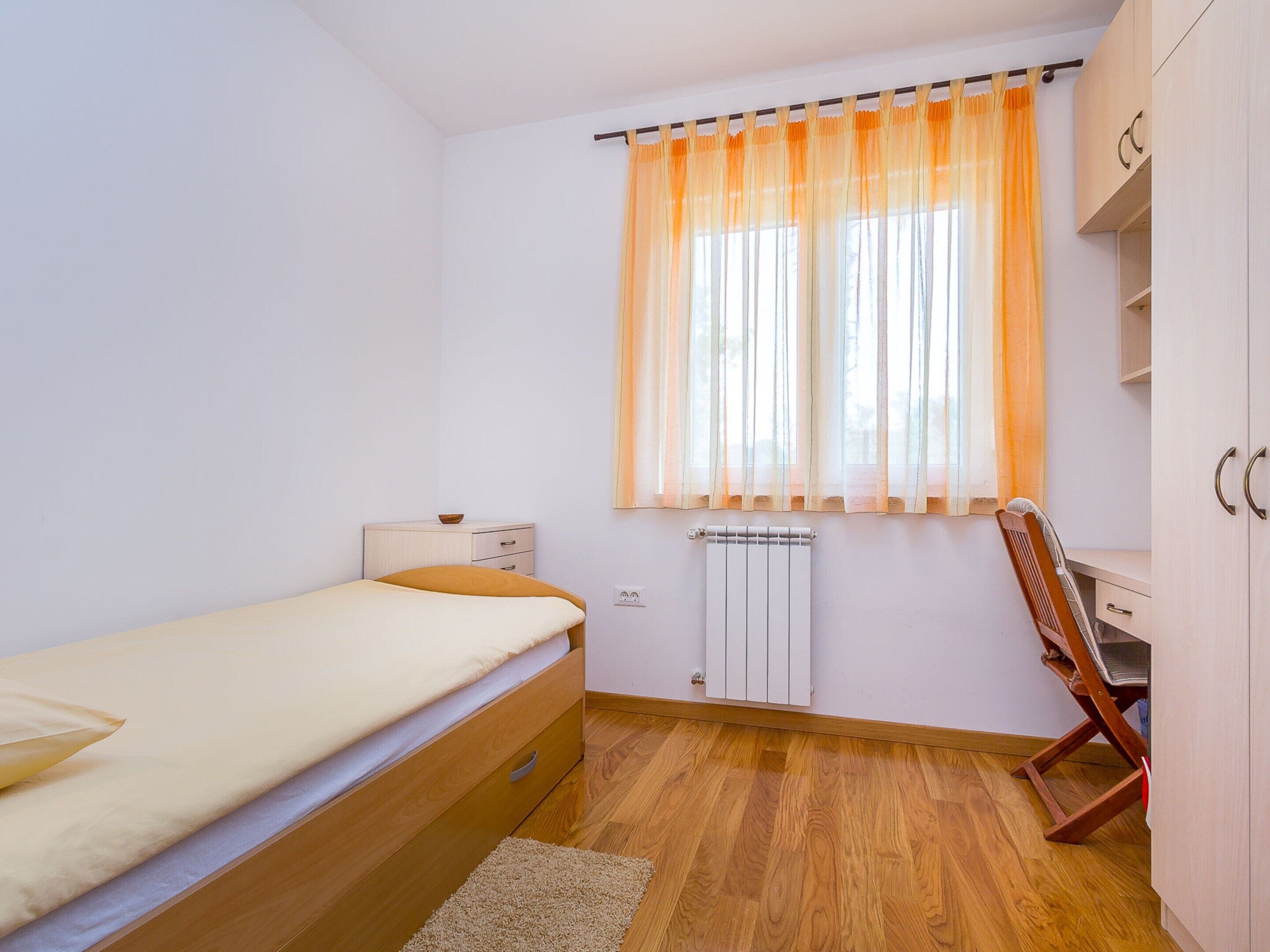 A small, well-lit room with a single bed, a wooden desk, and a radiator.
