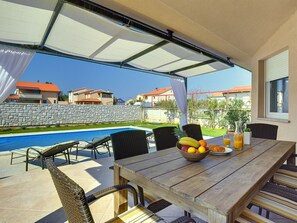 An outdoor patio with a pool, dining table, chairs, and a fruit bowl. - Modern Villa With Private Pool Near Beach (Fazana)