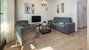 A modern living room with a grey sofa, patterned armchair, and a TV on a white stand. - Apartment in Pula Near the Sea and Town Center (Pula)
