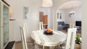 A dining area with a round table, white chairs, and a fruit bowl. There is a grey sofa and a TV in the background. - Apartment in Pula Near the Sea and Town Center (Pula)