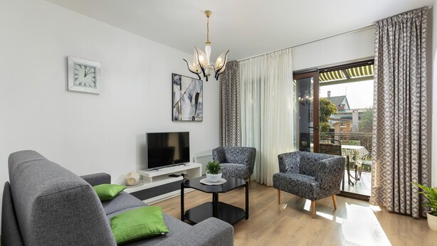 A modern living room with a grey sofa, two patterned armchairs, a flat-screen TV, a coffee table, and a chandelier. - Apartment in Pula Near the Sea and Town Center (Pula)