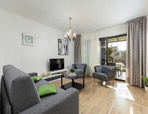 Una sala de estar moderna con un sofá gris, dos sillones estampados, un televisor de pantalla plana, una mesa de centro y una araña.