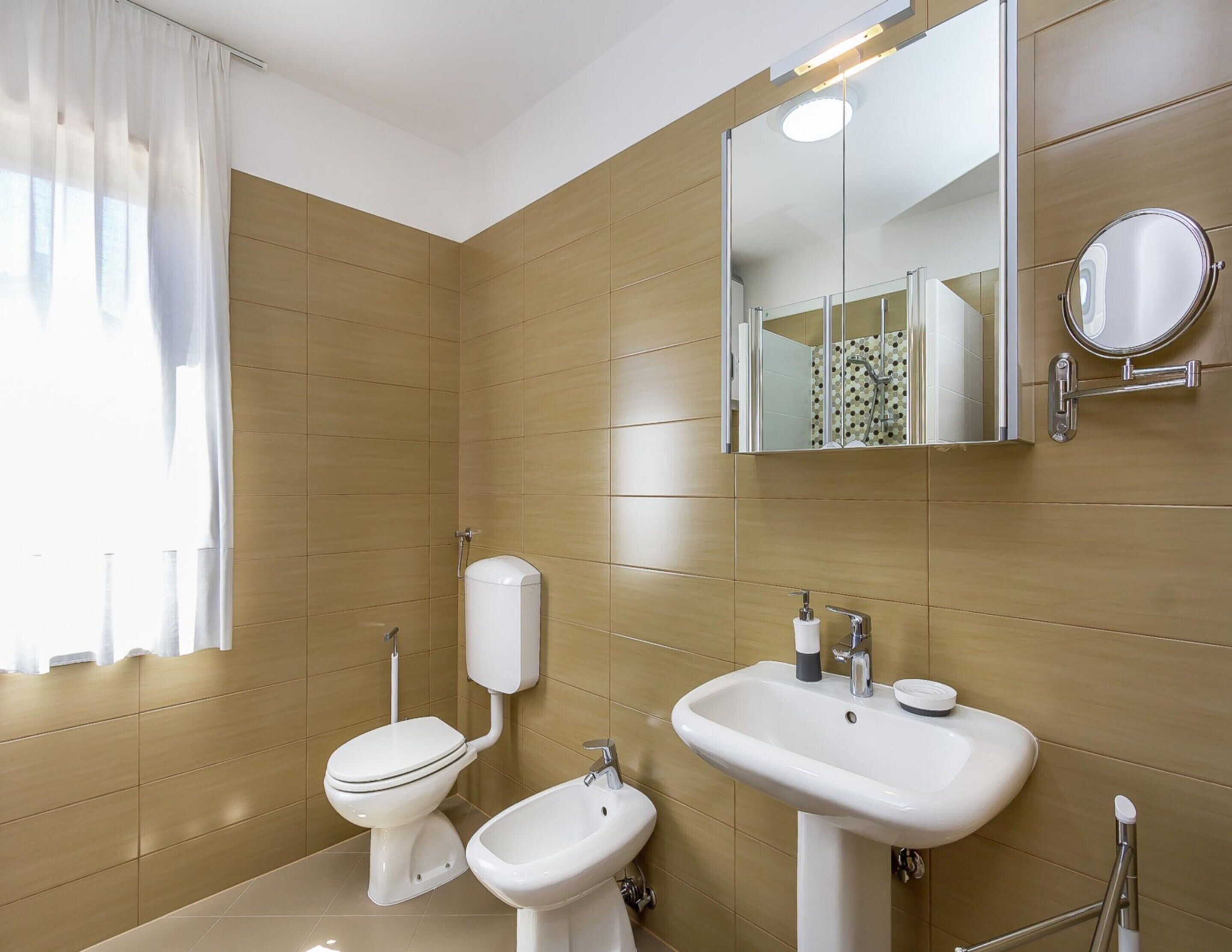 A modern bathroom with a toilet, bidet, and sink, wooden panel walls, and a large mirror.