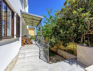 A staircase leading to a covered outdoor seating area with a table and chairs, surrounded by lush greenery and a stone wall. - Apartment in Pula Near the Sea and Town Center (Pula)