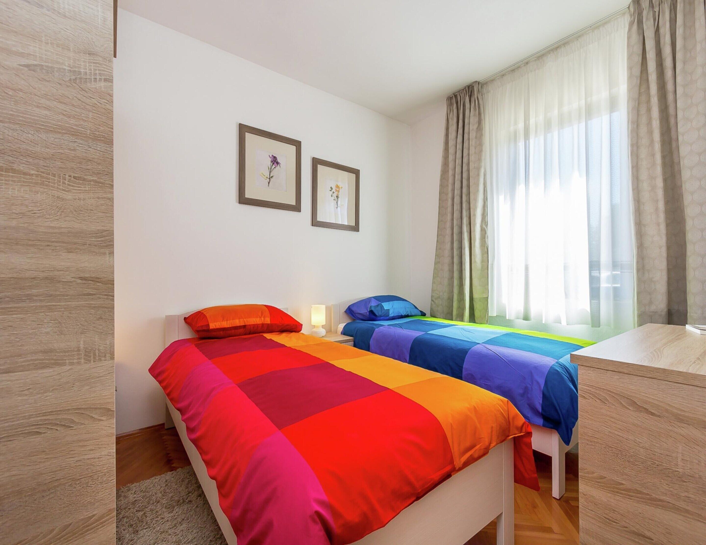 A bedroom with two beds, a desk, and a window with curtains.