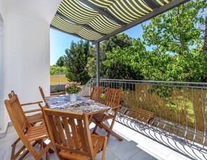 A covered outdoor seating area with a table and chairs, a view of greenery, and a metal railing. - Apartment in Pula Near the Sea and Town Center (Pula)