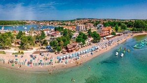 Vista aérea de un pueblo costero con playa, aguas claras y barcos.