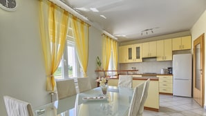 Una cocina moderna con armarios amarillos, una mesa de comedor de cristal y un refrigerador.