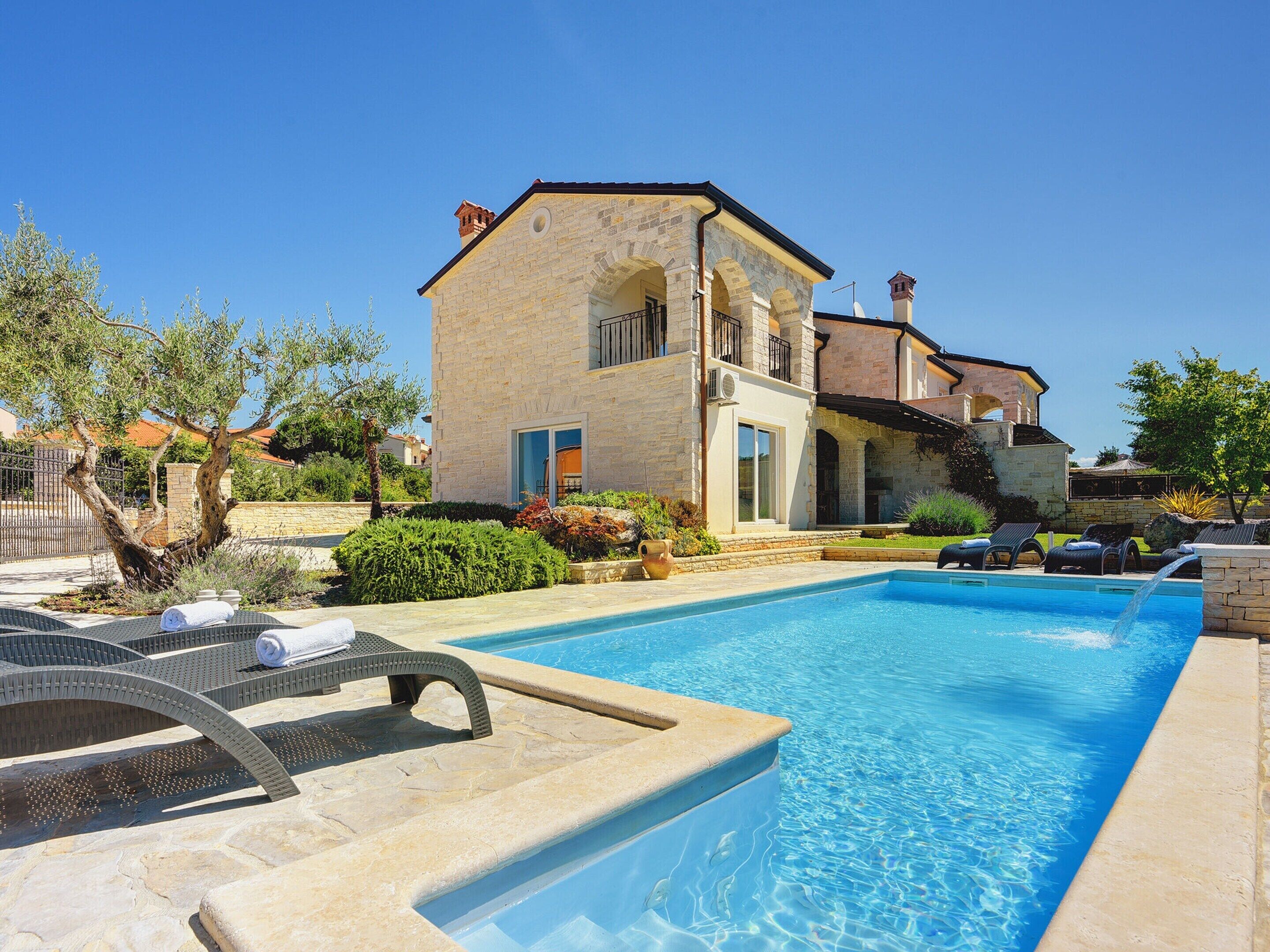A poolside area with lounge chairs, a stone building with arched windows, and a clear blue sky.