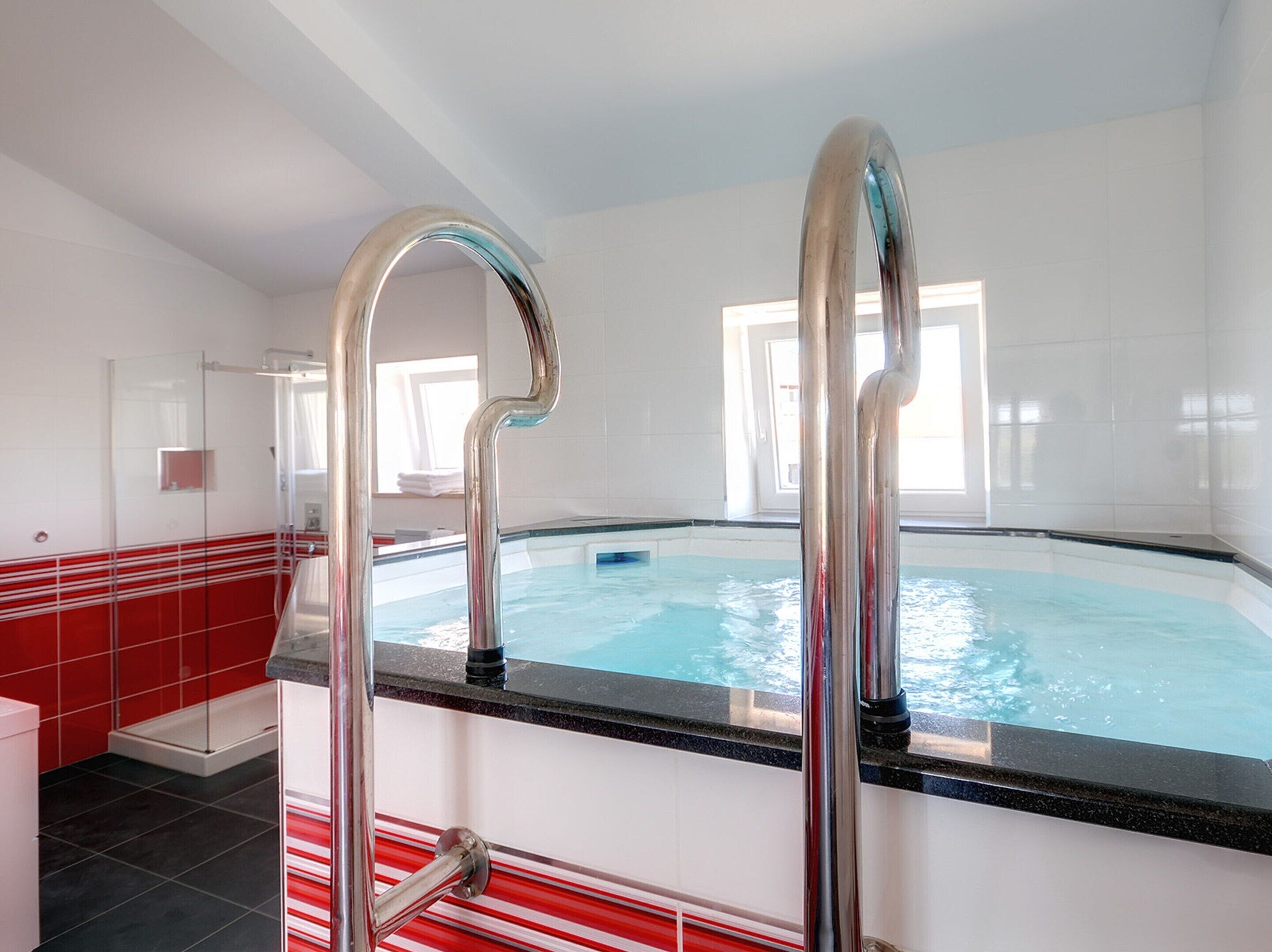 Una piscina amb paret de rajoles vermelles i blanques, un envàs de vidre i una escala metàl·lica.