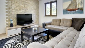 Un salon avec un mur en pierre, un téléviseur à écran plat, un canapé, une table basse et un tableau représentant un voilier.