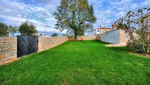 Un mur de pierre avec un portail noir, une cour gazonnée et un arbre.