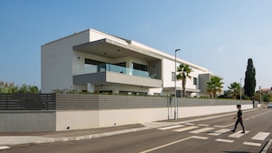 A modern two-story building with balconies, a pedestrian crossing, and a palm tree. - Apartment in Faana With Sea Beach (Fazana)