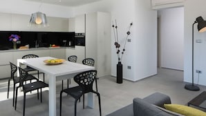 A modern kitchen with white cabinets, a dining table with chairs, and a vase with decorative branches. - Apartment in Faana With Sea Beach (Fazana)