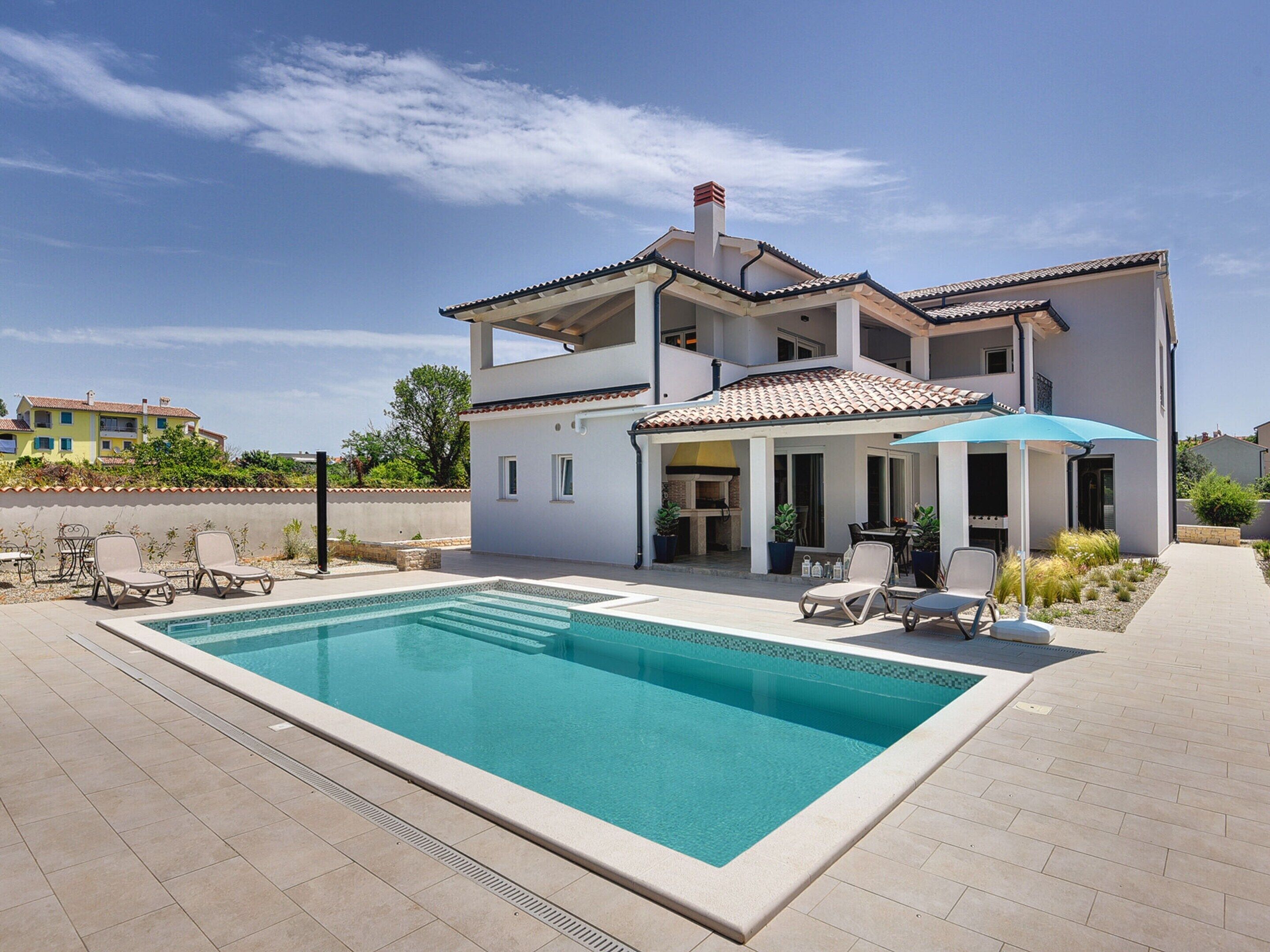 Una casa de dos pisos con piscina, mobiliario exterior y un patio cubierto.