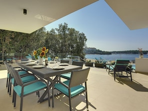 Enjoy a meal with a view of the sea from this outdoor dining area, featuring a table set with plates, glasses, and a vase with sunflowers.