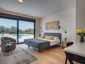 A modern bedroom with a large bed, a view of a swimming pool, and a dining area. - Villa in Vodnjan With Garden (Vodnjan)