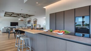 A modern kitchen with a central island, bar stools, and a built-in oven. - Villa in Vodnjan With Garden (Vodnjan)