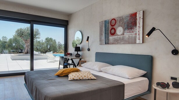 A modern bedroom with a large bed, a desk, and a view of a swimming pool. - Villa in Vodnjan With Garden (Vodnjan)