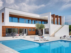 Una casa moderna de dos pisos con piscina, mobiliario exterior y una escalera que lleva al nivel superior.