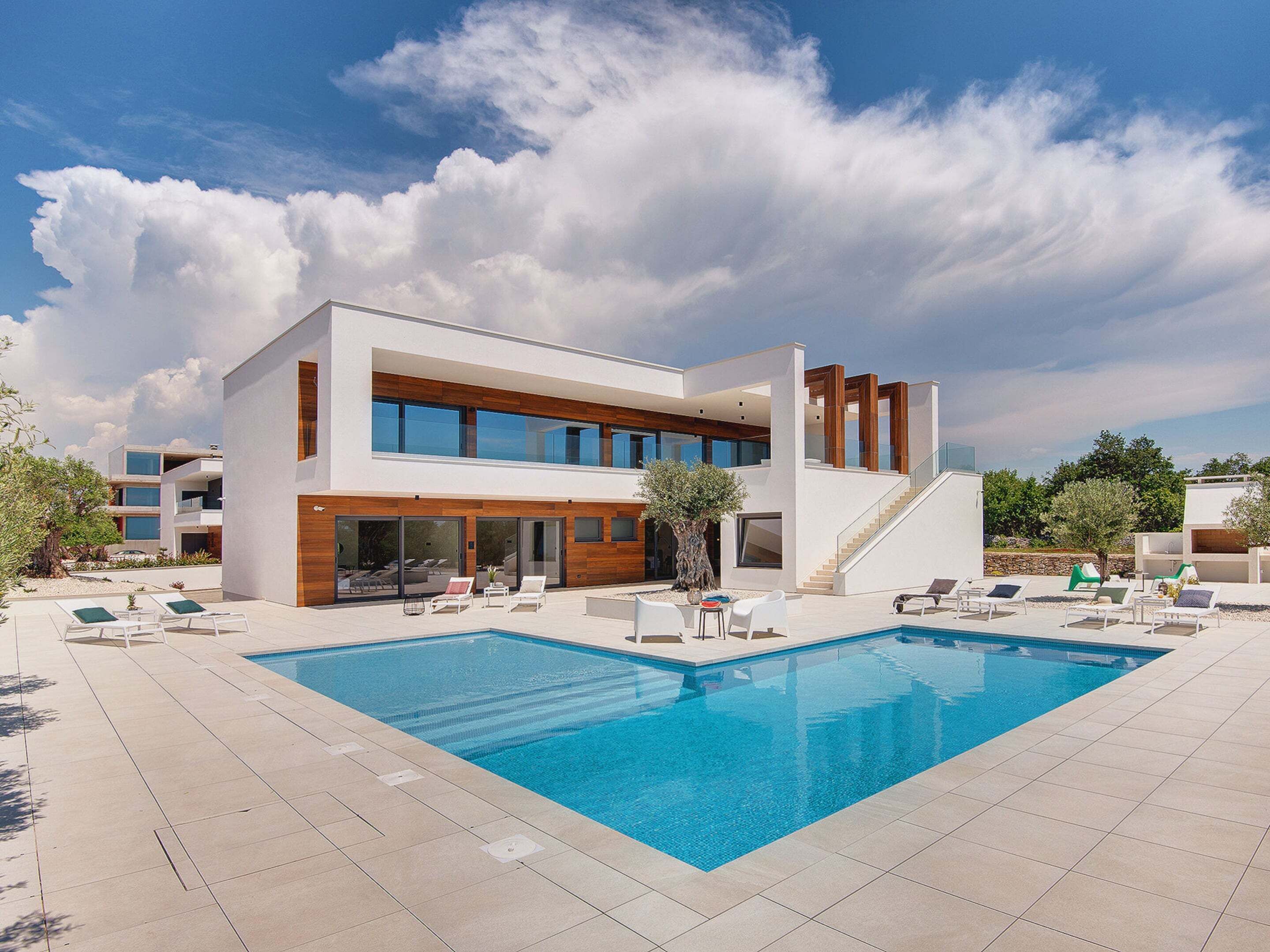 A modern two-story building with a swimming pool, lounge chairs, and a staircase leading to an upper level.