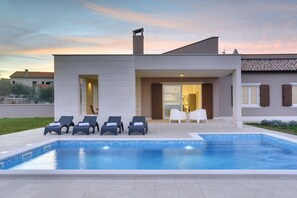 Une maison moderne dotée d’une piscine, d’un espace salon extérieur et d’un patio.