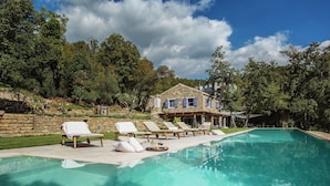 Un espace piscine avec des chaises longues et, en arrière-plan, une maison en pierre.