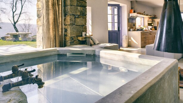 Un espace spa moderne avec un mur en pierre, un jacuzzi entouré de parois de verre et une vue sur la cuisine et la salle à manger.