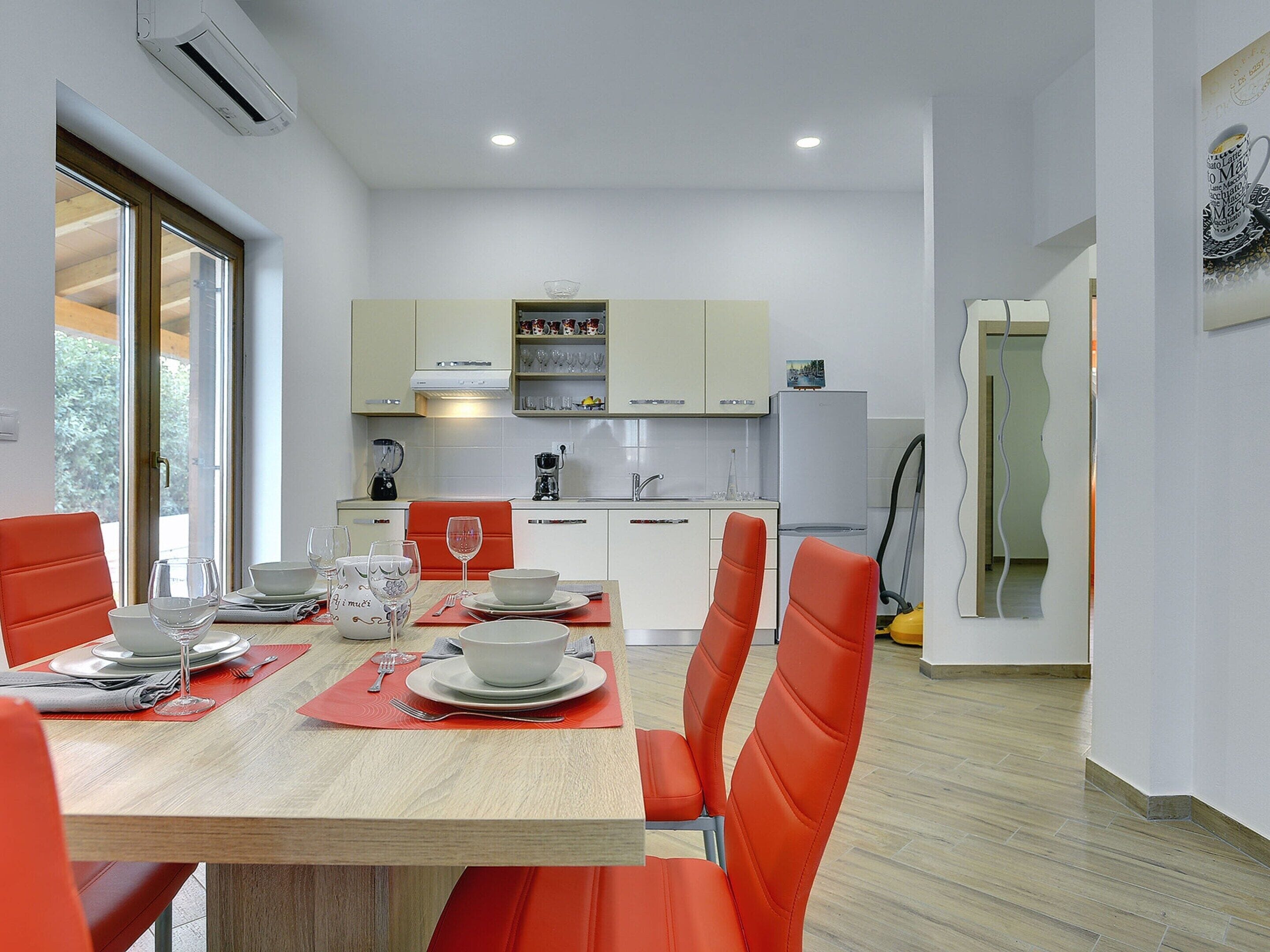 A modern kitchen with white cabinets, a dining table set with plates, glasses, and a red chair.