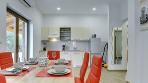 A modern kitchen with white cabinets, a dining table set with plates, glasses, and a red chair. - Detached Modern Villa With Pool and Fenced Yard Near the Sea (Liznjan)