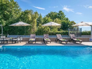 Ein Swimmingpool mit Liegestühlen und Sonnenschirmen, umgeben von Bäumen.