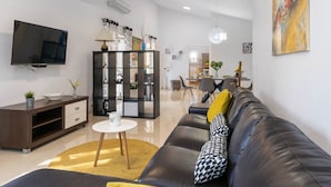 A modern living room with a black leather sofa, a television, a black shelving unit, and a dining area in the background. - Detached Holiday Home With Swimming Pool, Near the Beach (Marcana)
