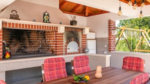 An outdoor patio with a brick barbecue, seating with plaid cushions, and hanging light bulbs. - Detached Holiday Home With Swimming Pool, Near the Beach (Marcana)