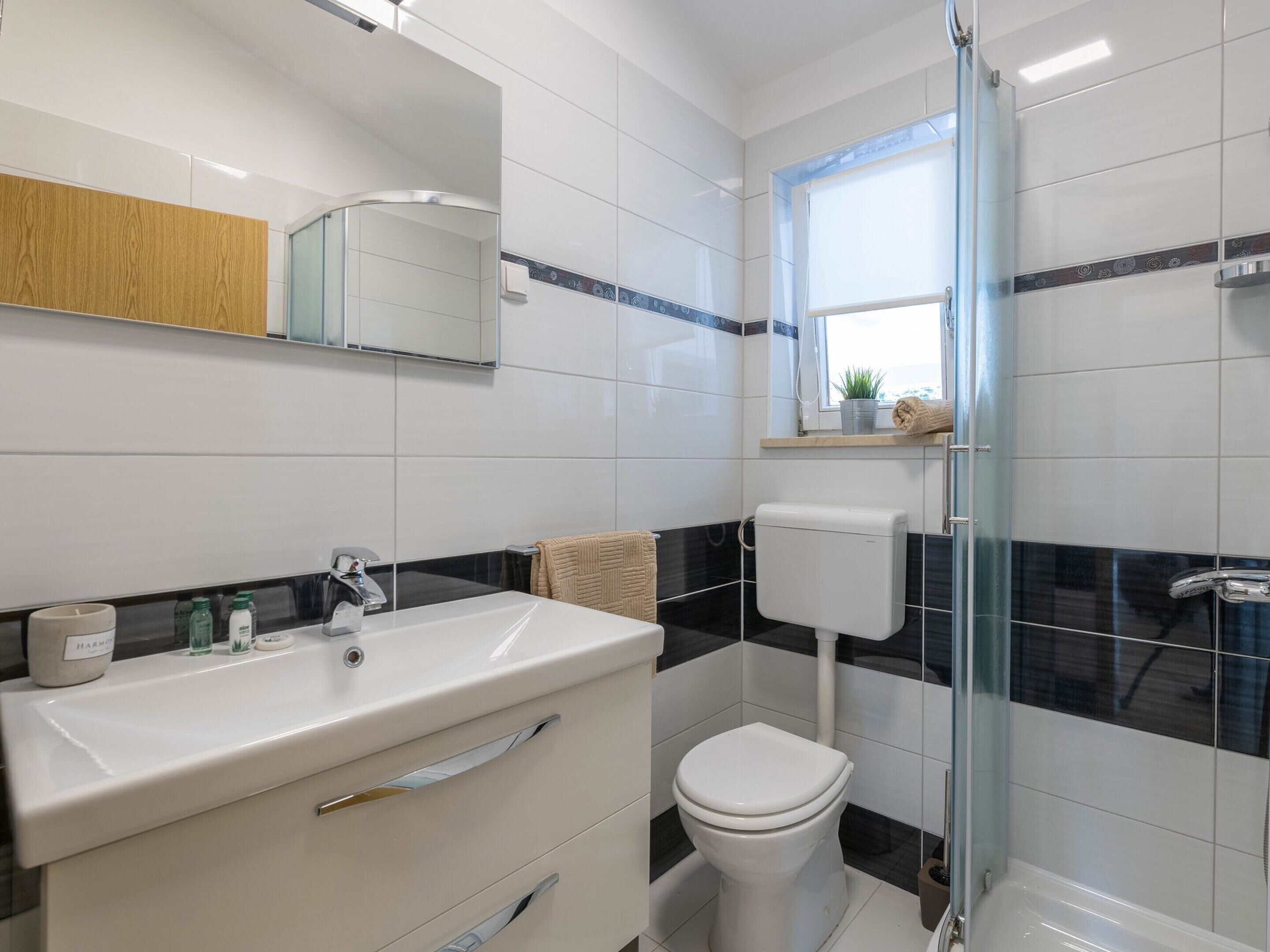 Een badkamer met een wit wastafelmeubel, een toilet en een douchecabine met glazen wanden.