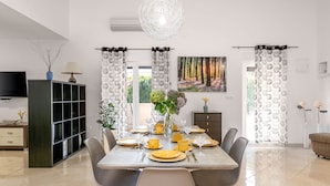 A modern dining area with a grey table set for four, surrounded by grey chairs with wooden legs. A large, round chandelier hangs above the table. - Detached Holiday Home With Swimming Pool, Near the Beach (Marcana)