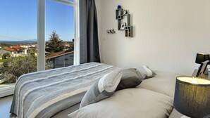 A bedroom with a large window, a bed with striped bedding, a bedside lamp, and a wall-mounted shelf with a clock and picture frame. - Villa in Liznjan With Pool Near the Beach (Liznjan)