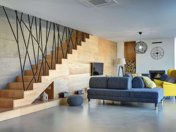 A modern living room with a wooden staircase, a sofa set, and a fireplace.
