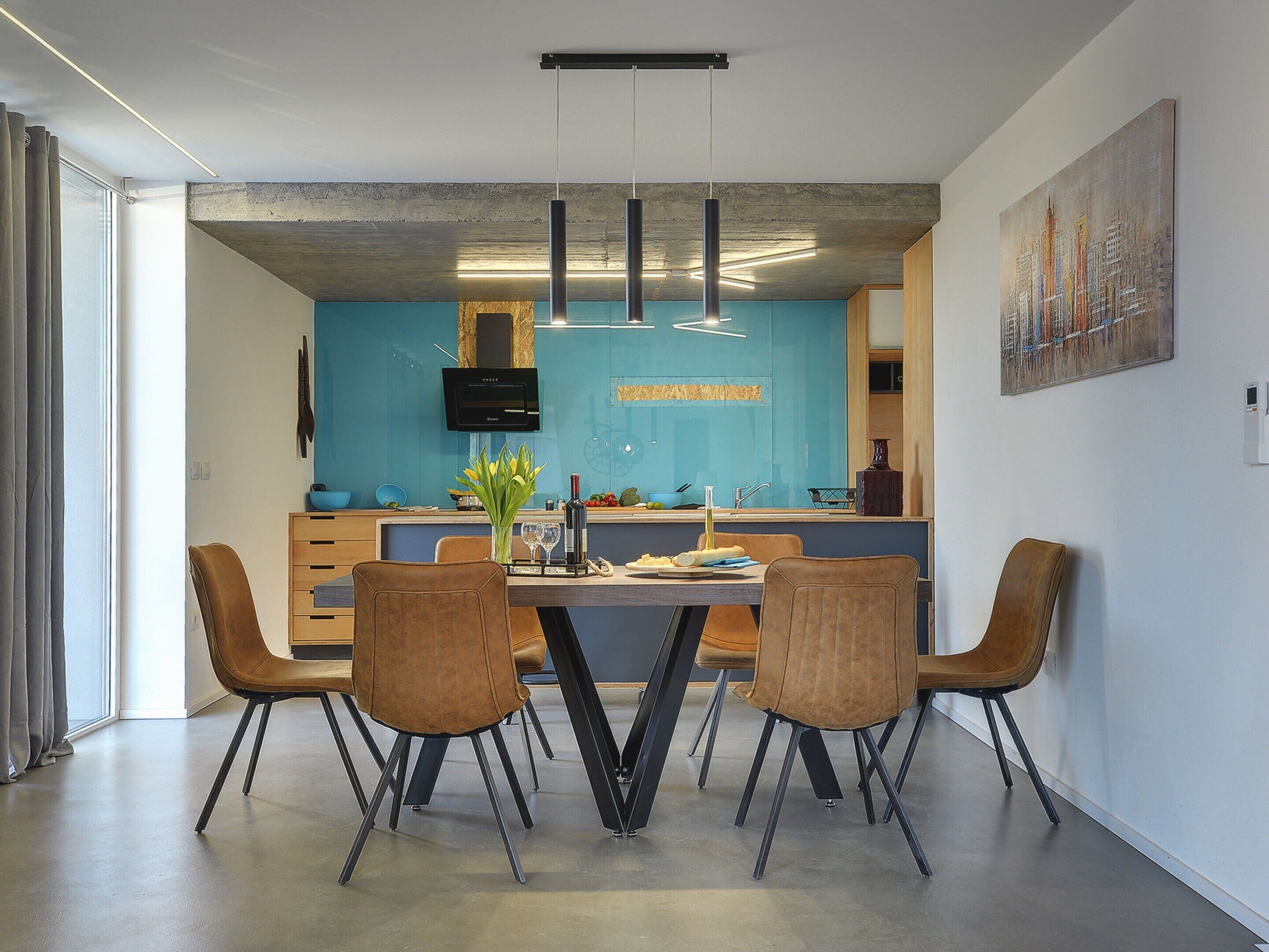 A modern kitchen with a blue backsplash, a dining area with a table and chairs, and a large painting on the wall.