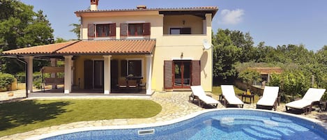 A two-story house with a swimming pool, a covered patio, and a garden.