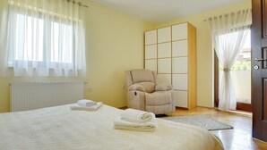 Et soveværelse med seng, stol, garderobe og et vindue med gardiner.