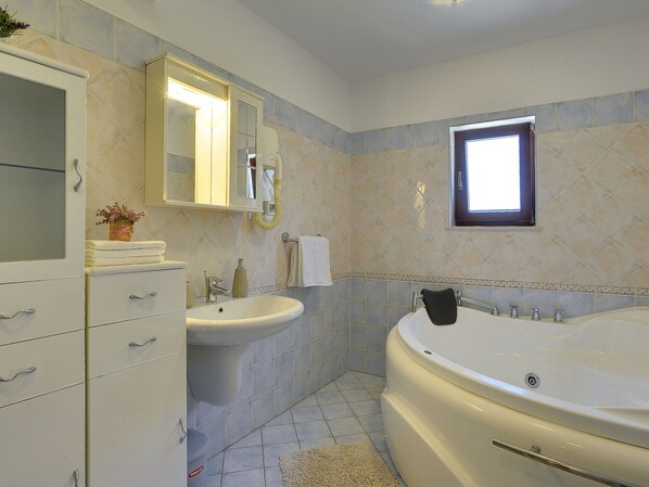 Un baño con bañera, dos lavamanos, tocador con cajones, espejo y ventana.