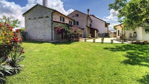 A stone house with a garden, a white building with a chimney, and a tree with pink flowers. - Holiday Home in Rojnici With Private Pool (Barban)